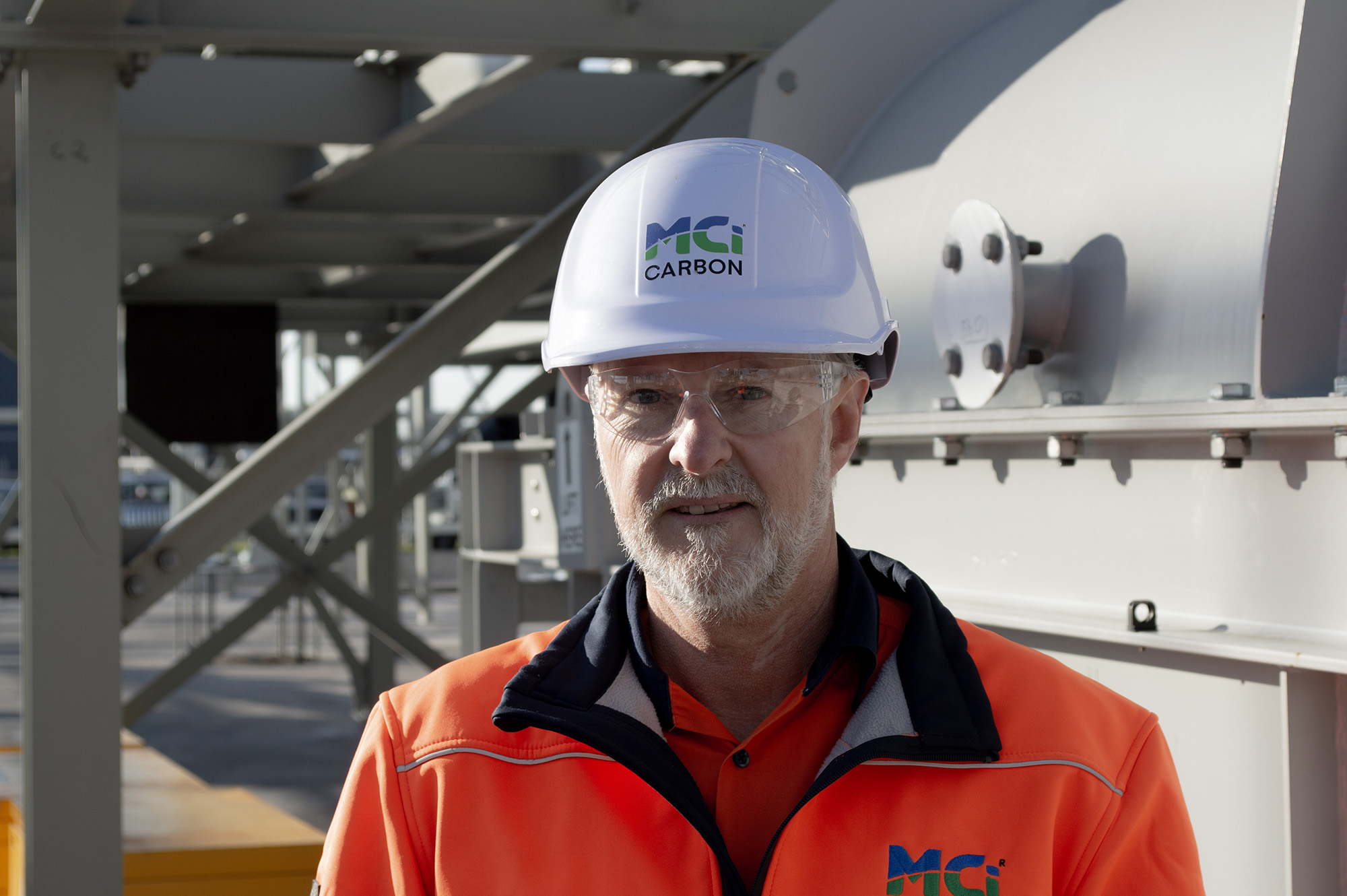 A man in hi-vis and a helmet with 'MCi Carbon' stands in an industrial setting.