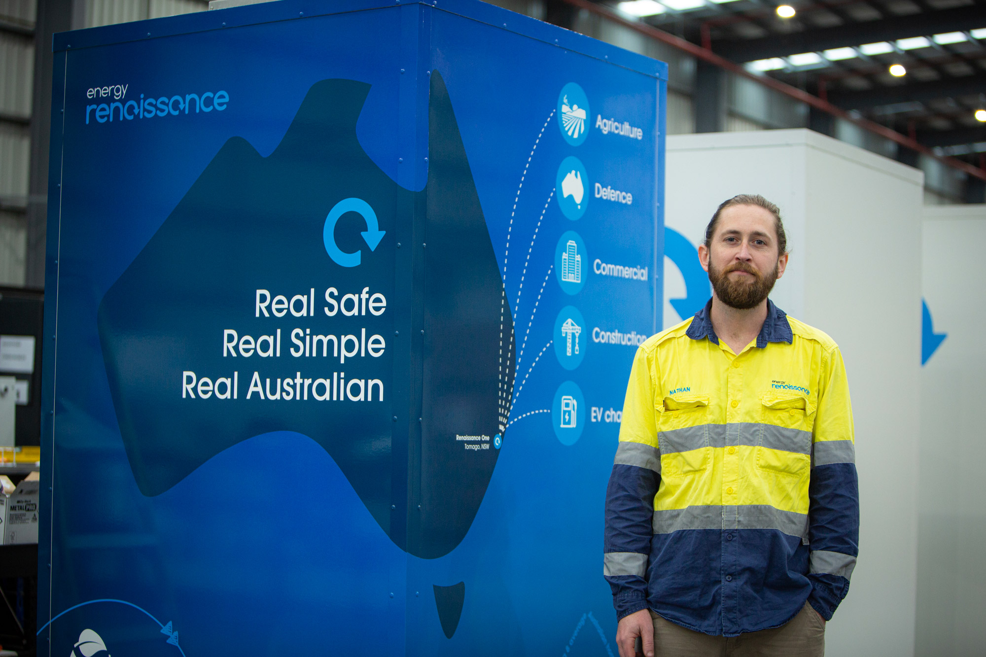 A man in hi-vis stands in front of an Energy Renaissance sign which says 'Real Safe, Real Simple, Real Australian'.