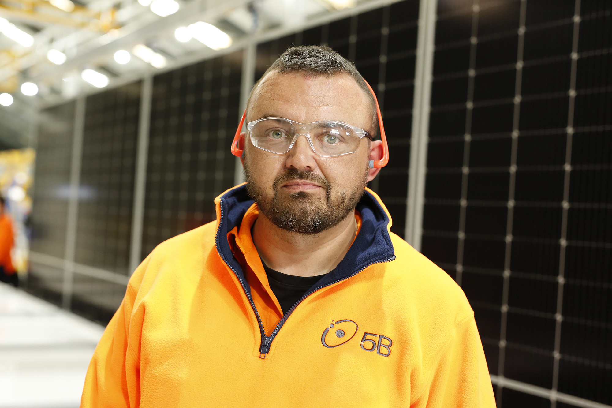 A man in hi-vis stands in front of a solar panel at a manufacturing plant.