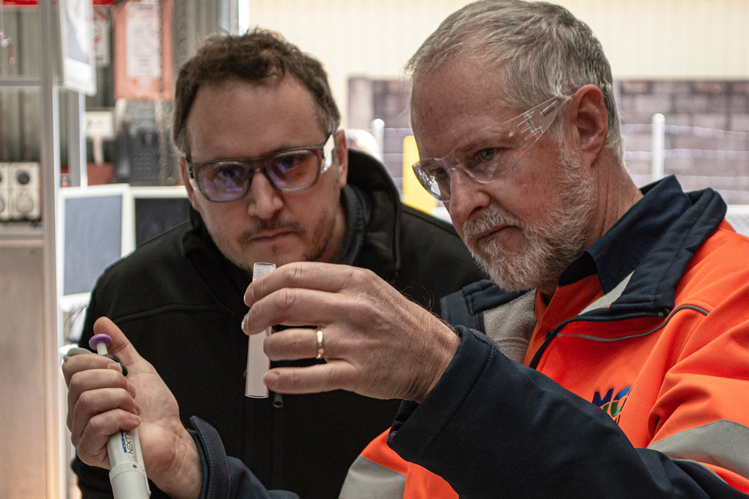 A man in hi-vis analyses two test tubes along with his male coworker.