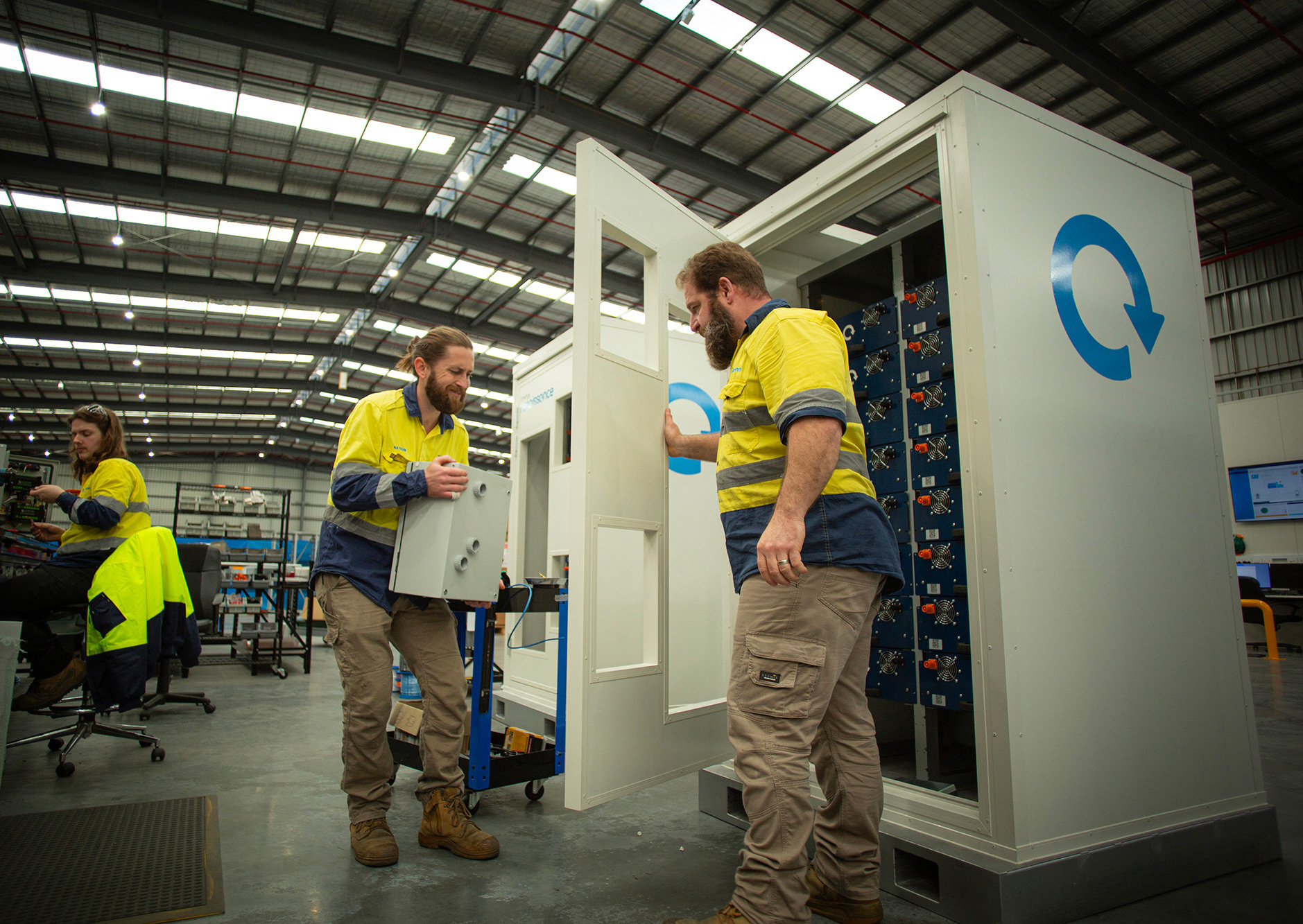 A man in hi-vis lifts a large battery with his male coworker in a battery manufacturing plant.